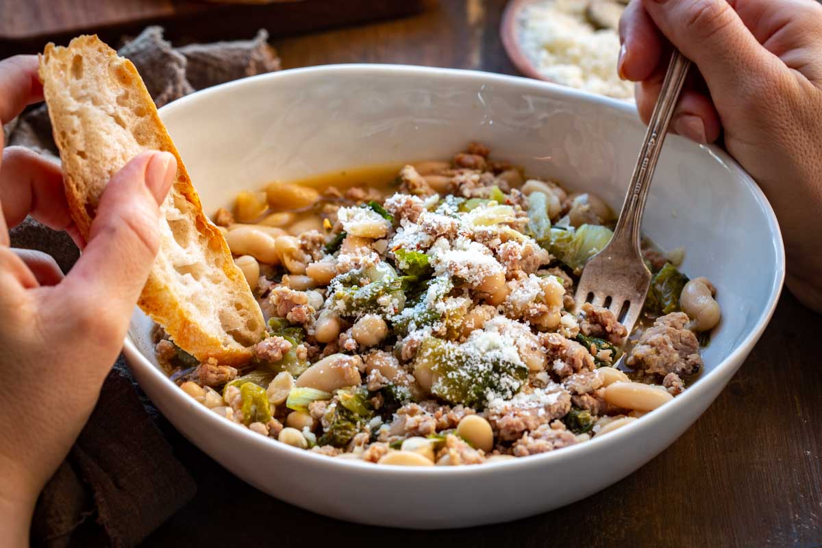 Overhead view of the finished stew showing tender beans, wilted escarole, and sausage in broth.
