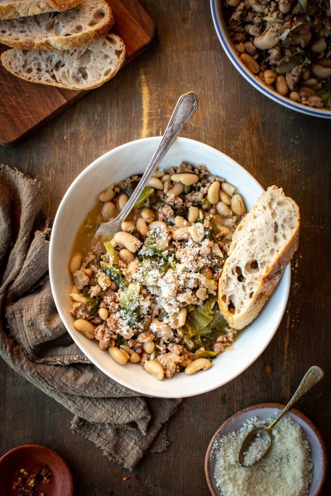 A bowl of sausage, escarole, and white bean stew with bread for dipping.