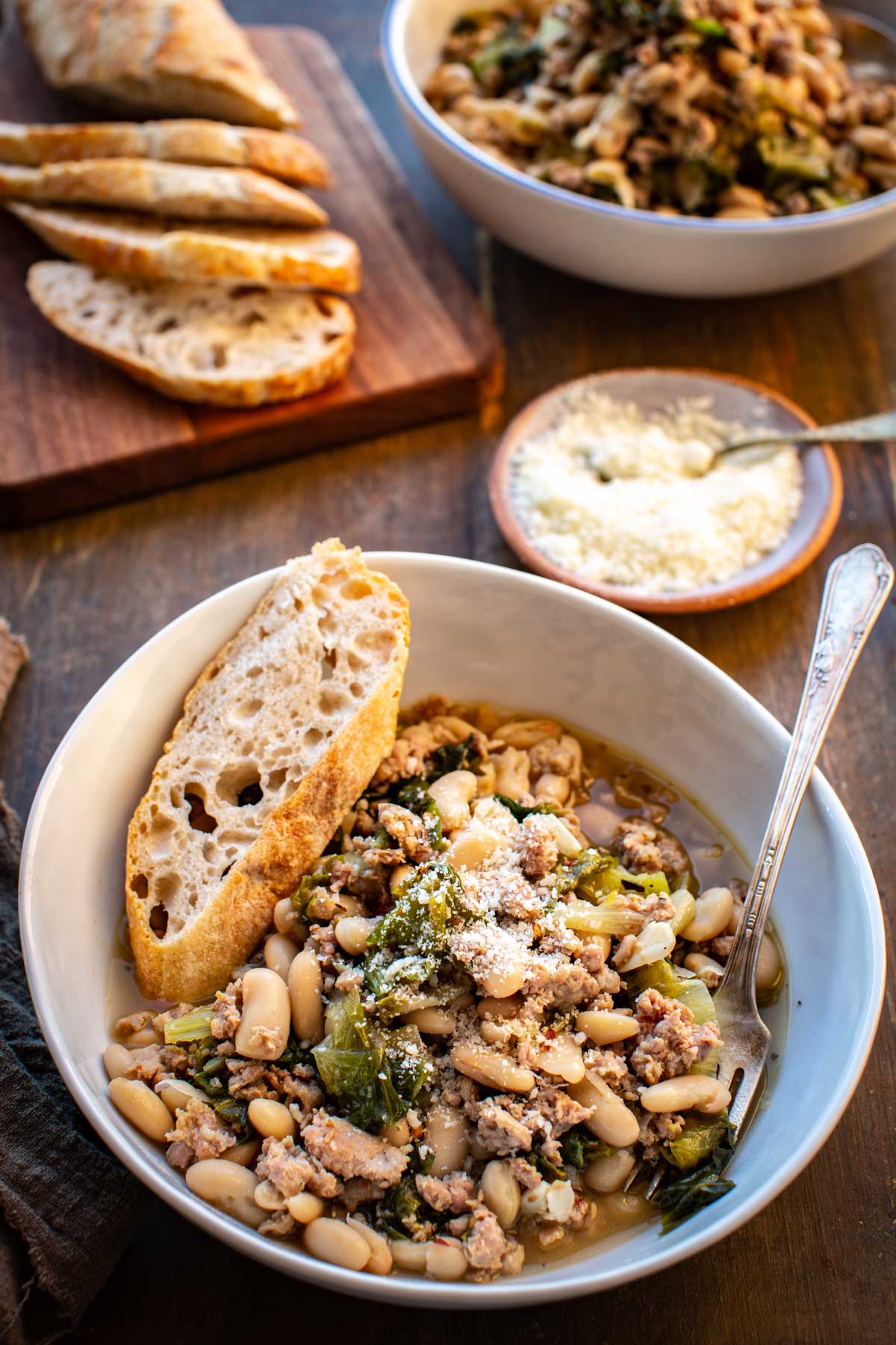 Bowl of sausage, escarole, and white bean stew topped with grated Pecorino Romano and served with crusty bread.