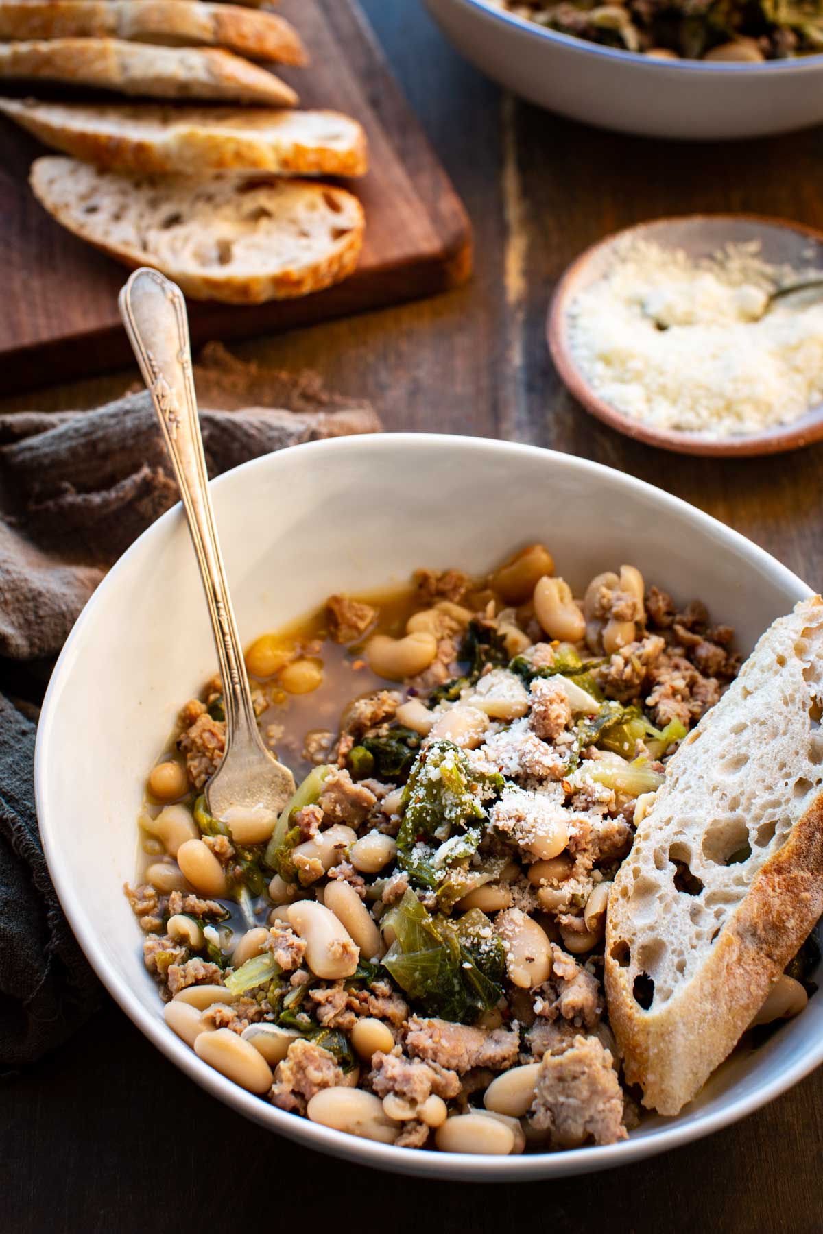 Close up of the finished stew in a white bowl with a slice of rustic bread resting on the edge.