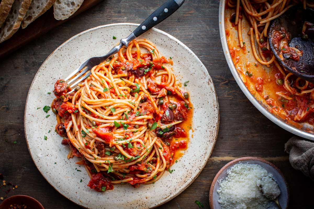 Spaghetti puttanesca served on a plate with visible olives, capers, and tomato sauce.