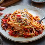 Close up of spaghetti puttanesca showing strands of pasta coated in tomato sauce with olives and capers.