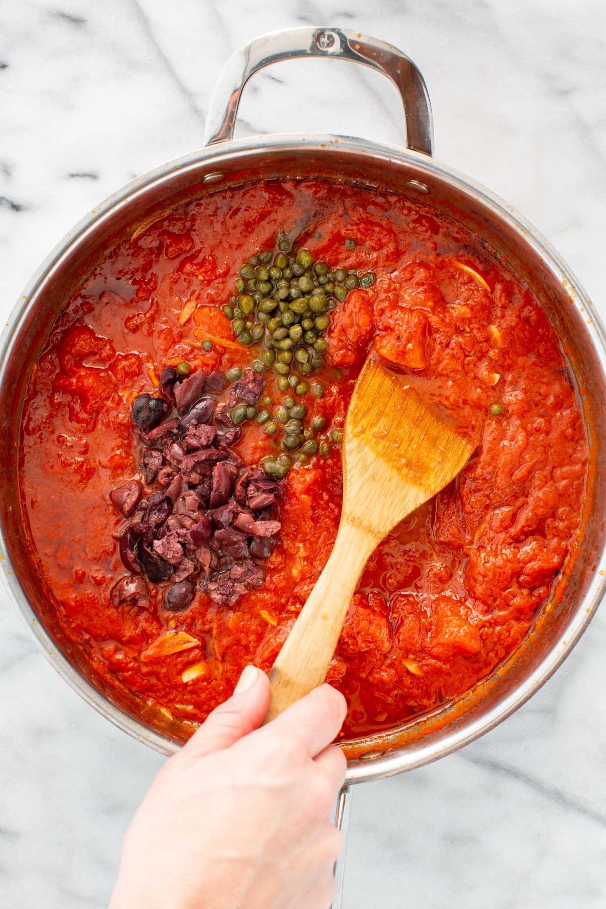 Chopped olives and capers added to the simmering tomato sauce before stirring.