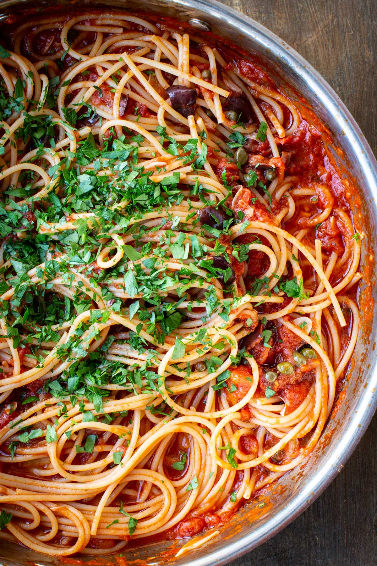 Finished spaghetti puttanesca topped with chopped fresh parsley in the pan.