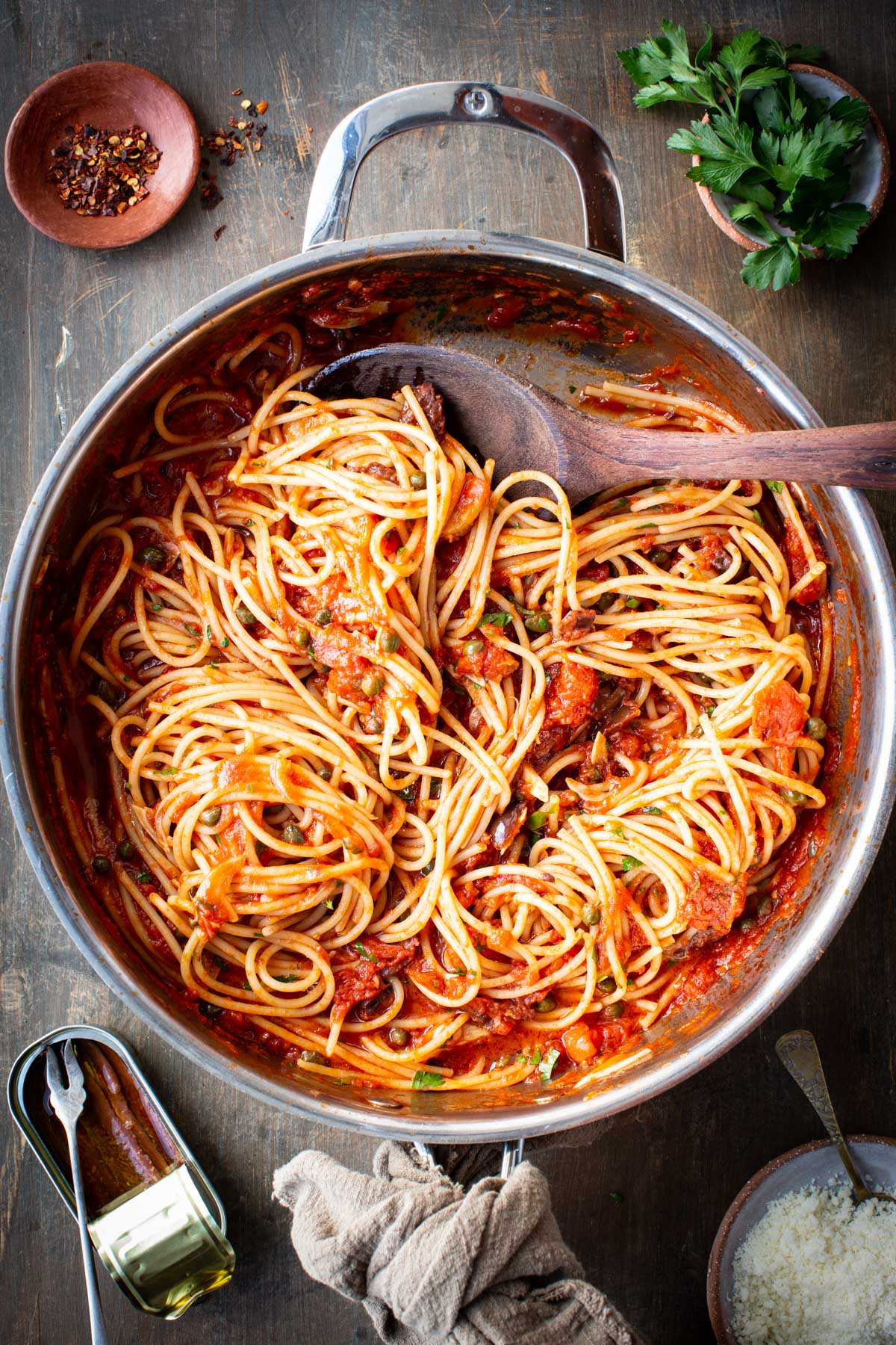 Spaghetti fully coated in puttanesca sauce with olives and capers evenly distributed.