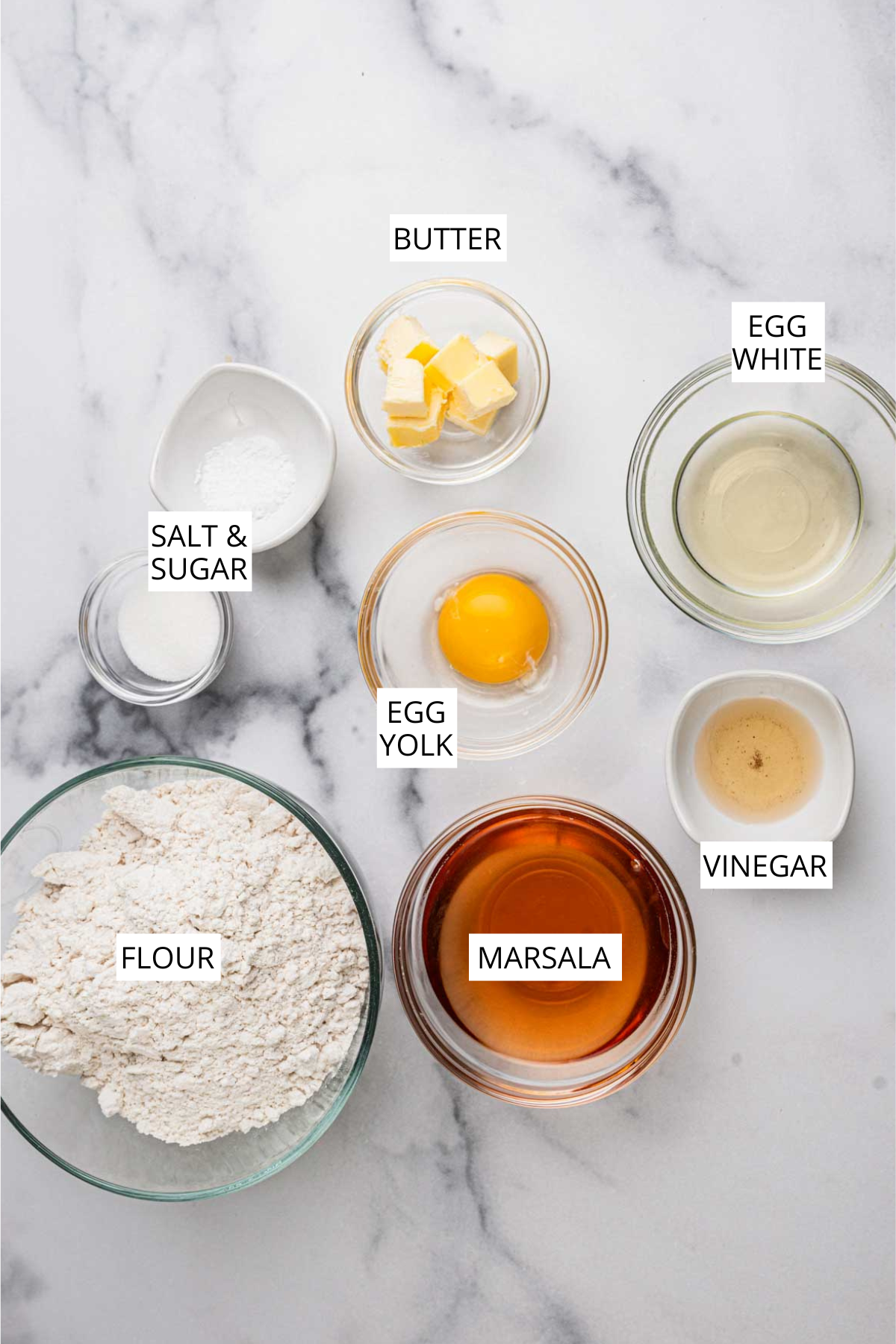 Cannoli shell ingredients layed out in a white marble background.