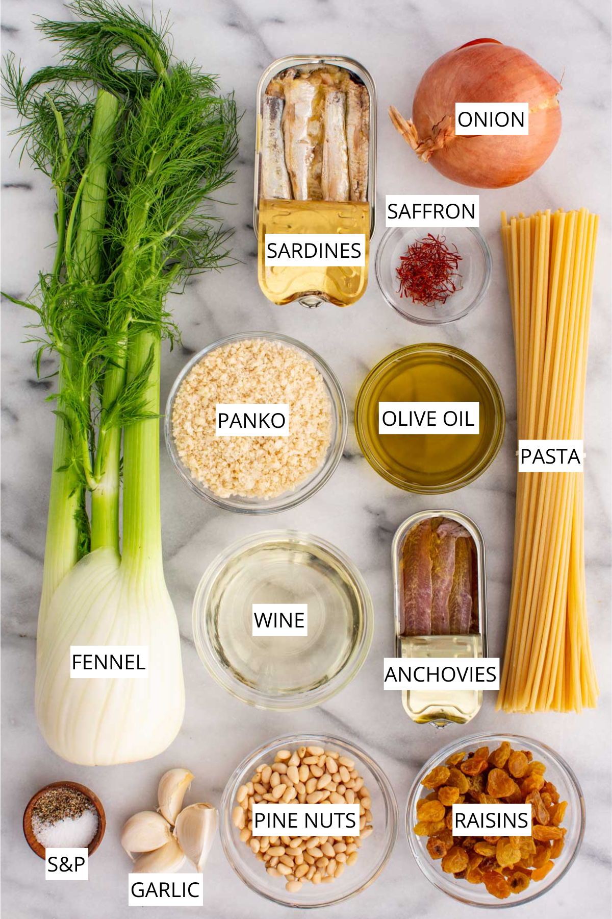 Ingredients for pasta con le sarde arranged on marble, including fennel, canned sardines, anchovies, spaghetti, onion, garlic, olive oil, white wine, pine nuts, raisins, panko breadcrumbs, saffron, salt and pepper.