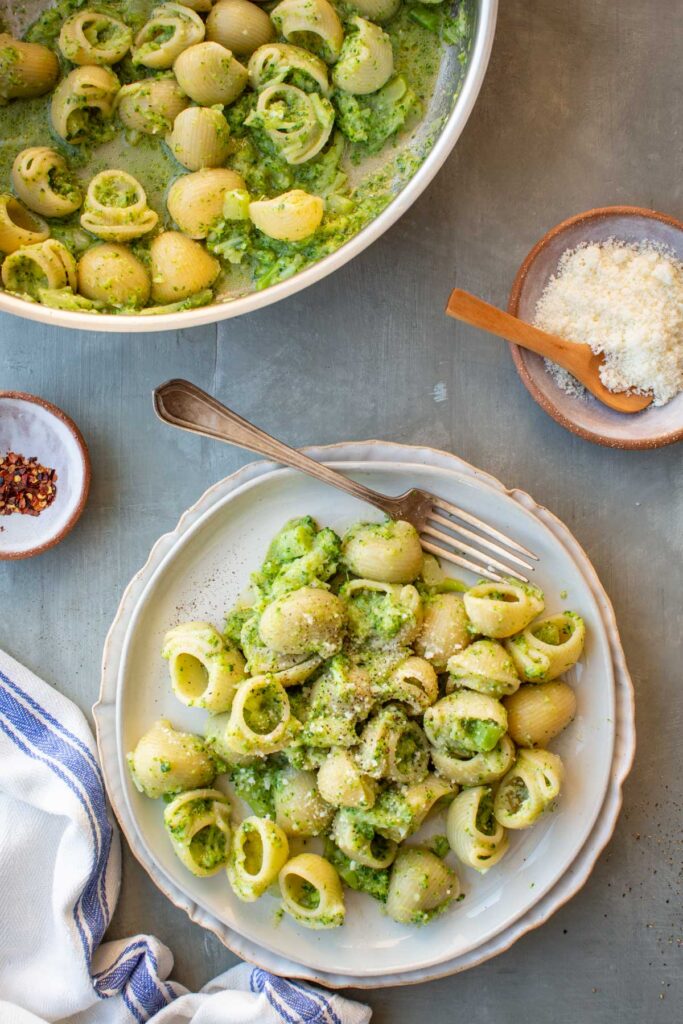 Overhead view of pasta con broccoli served in a shallow bowl, with shell pasta coated in a creamy mashed broccoli sauce and topped with grated cheese and black pepper.