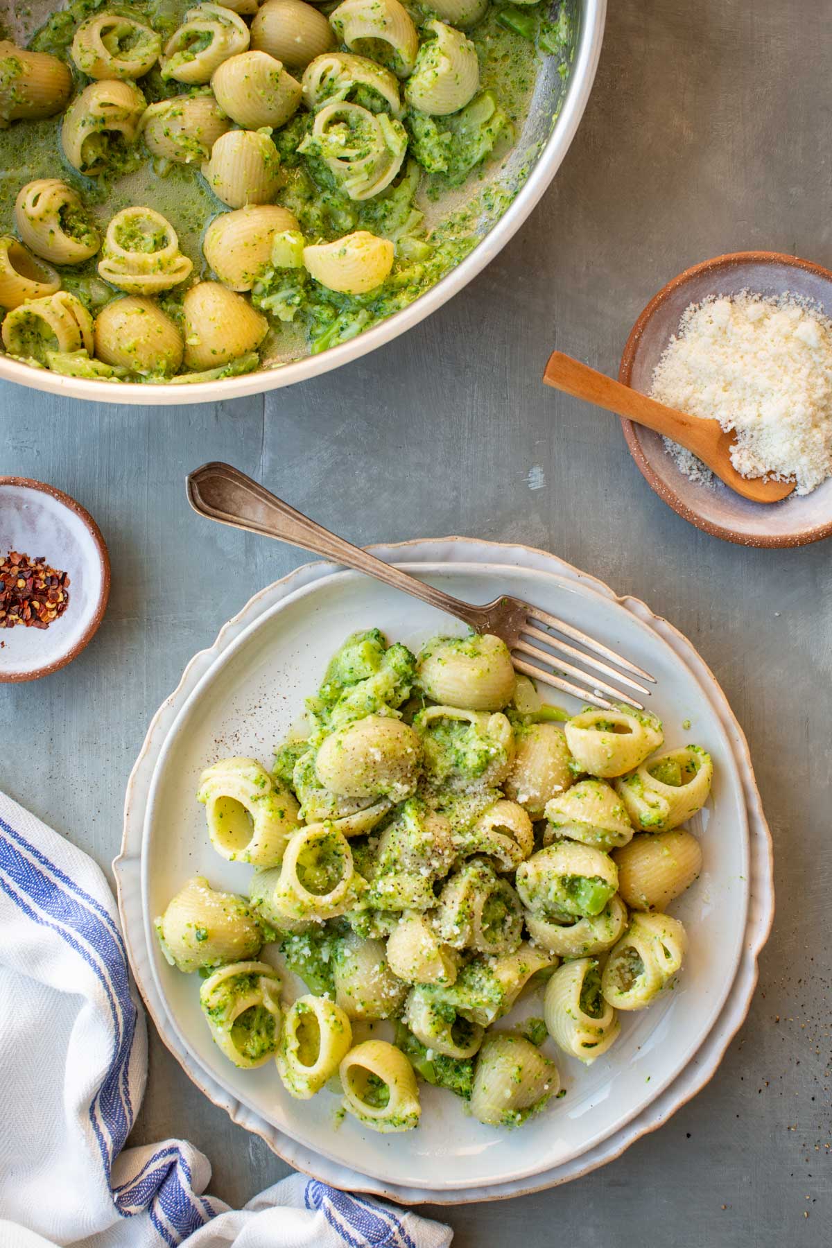 Overhead view of pasta con broccoli served in a shallow bowl, with shell pasta coated in a creamy mashed broccoli sauce and topped with grated cheese and black pepper.