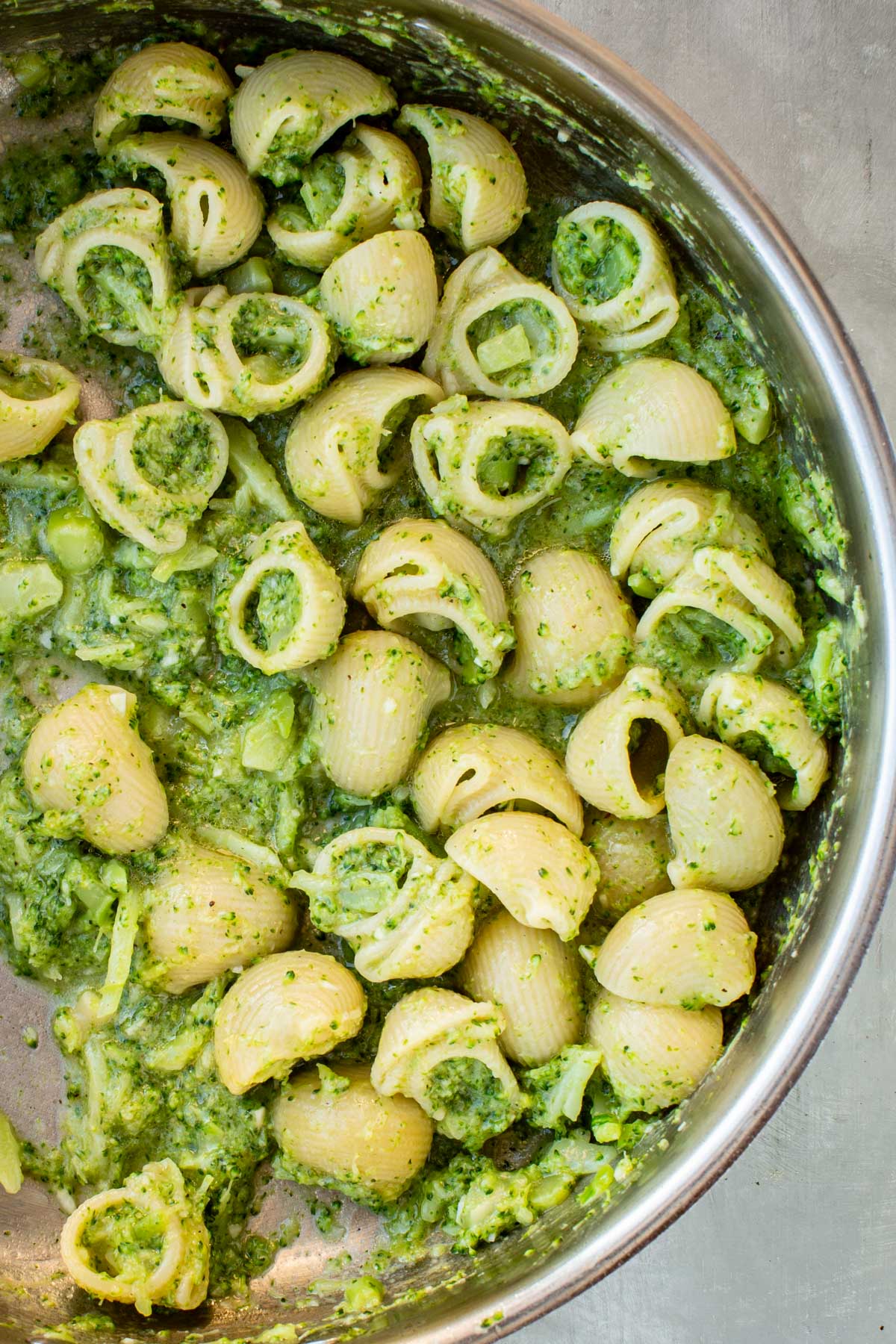 Close up of shell pasta tossed with tender broccoli and a glossy green sauce in a stainless steel skillet.
