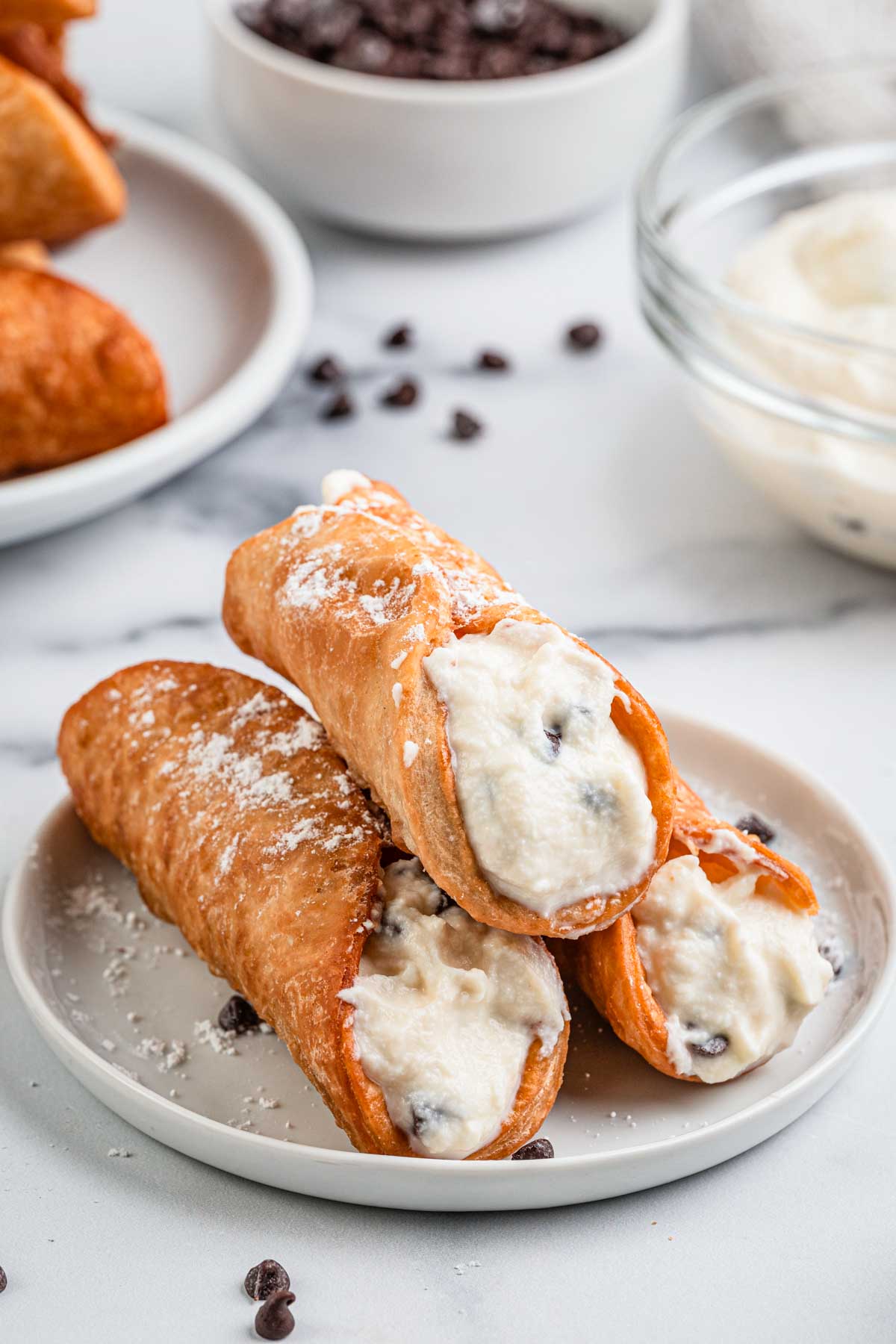 Crispy cannoli shell filled with creamy ricotta and chocolate chips, dusted with powdered sugar.