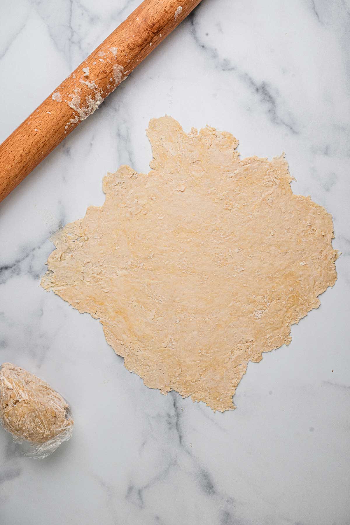 Cannoli dough rolled until thin with a rolling pin in a white marble background.