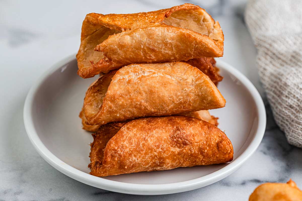 Golden fried cannoli shells stacked on a small white plate, showing their crisp texture.