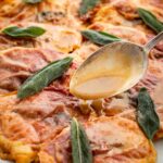 Detailed close-up of chicken saltimbocca with crisped prosciutto and sage leaves, finished with a spoonful of silky pan sauce.