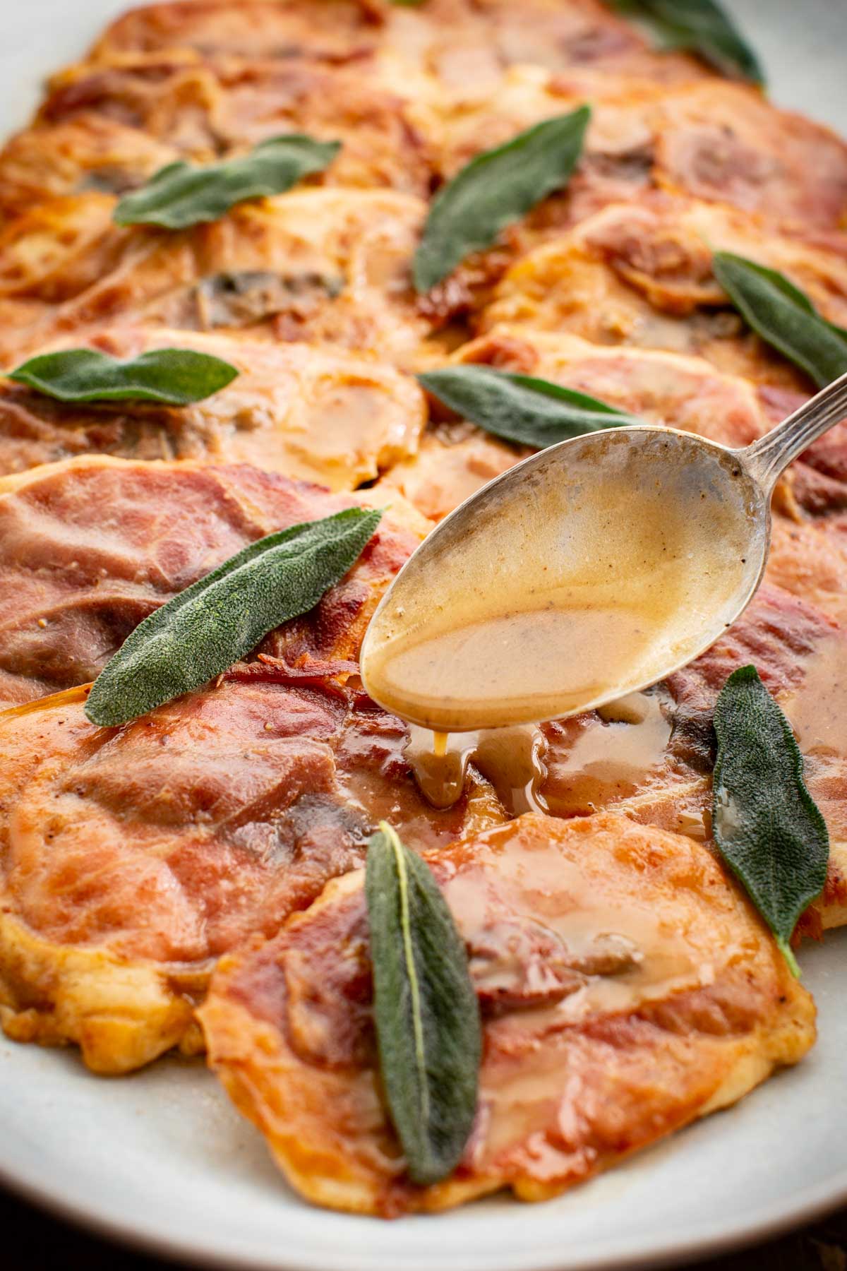 Detailed close-up of chicken saltimbocca with crisped prosciutto and sage leaves, finished with a spoonful of silky pan sauce.