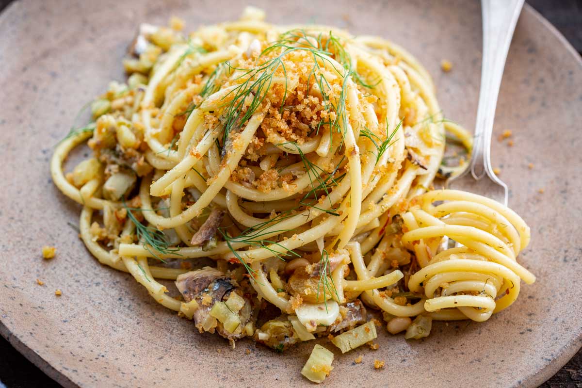 Detailed close up of a forkful of pasta con le sarde with toasted breadcrumbs and fresh fennel fronds on top.