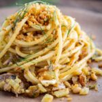 Close up of pasta con le sarde showing spaghetti mixed with sardines, diced fennel, pine nuts, raisins and saffron breadcrumbs.