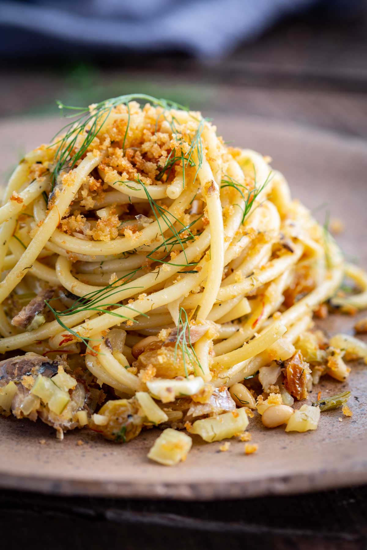 Close up of pasta con le sarde showing spaghetti mixed with sardines, diced fennel, pine nuts, raisins and saffron breadcrumbs.