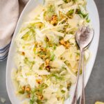 Top shot of plated shaved fennel salad with next to serving spoons and cloth napkins.
