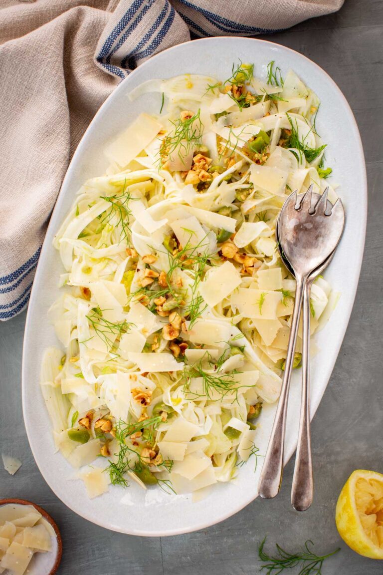 Top shot of plated shaved fennel salad with next to serving spoons and cloth napkins.