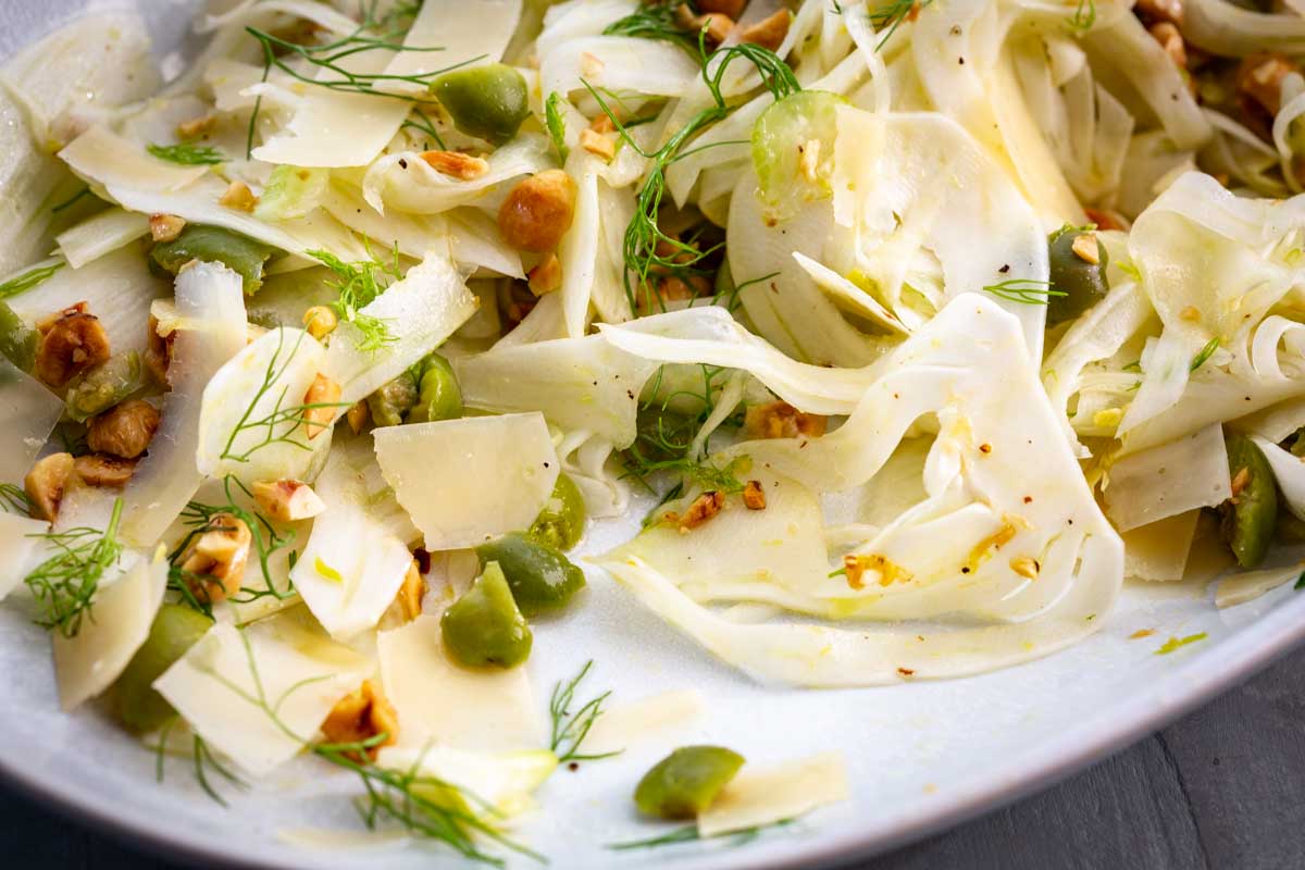Side view of of shaved fennel salad with visible olives, fennel fronds and hazelnuts.