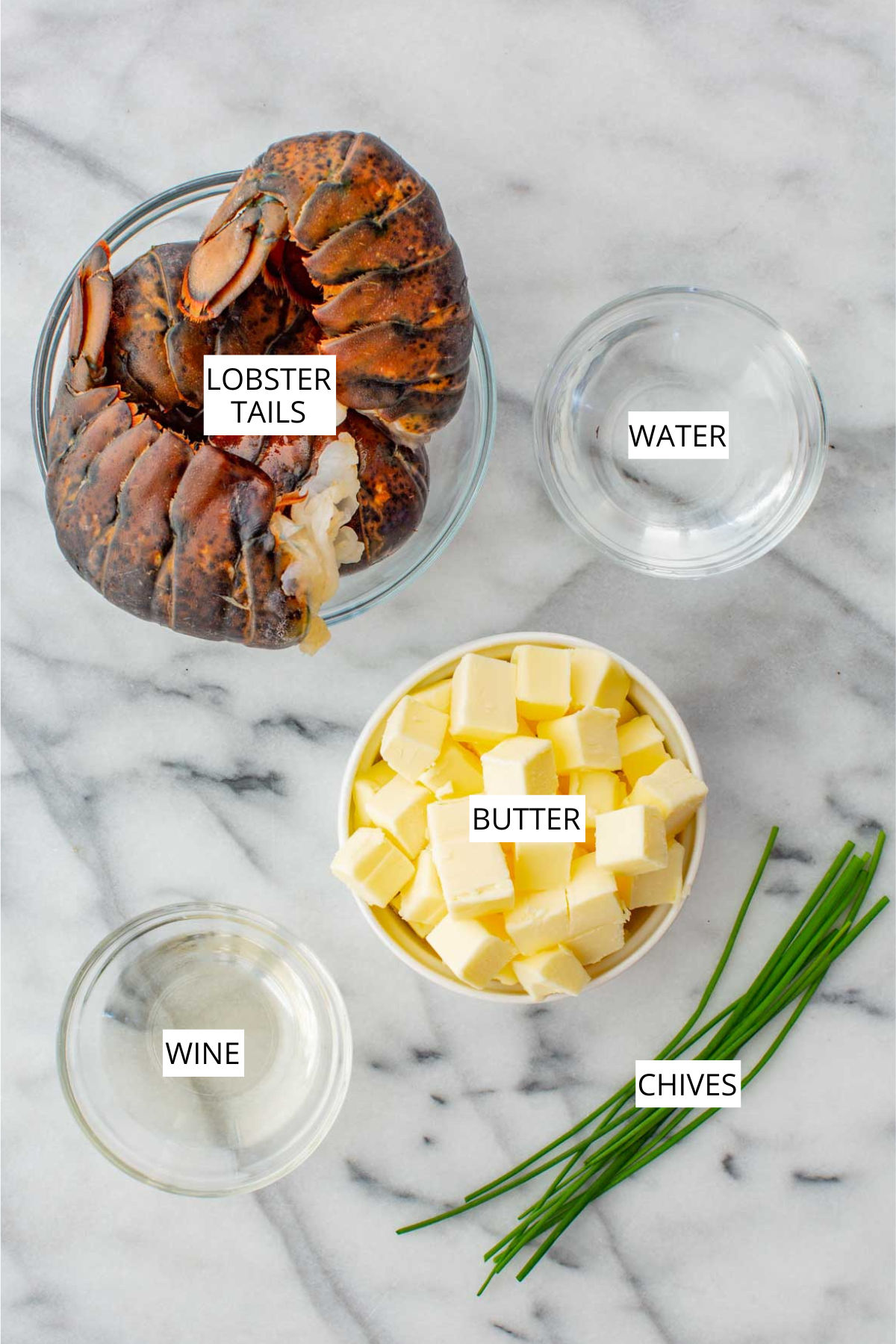 Labeled ingredients of butter poached lobster including lobster tails, wine, butter and chives.