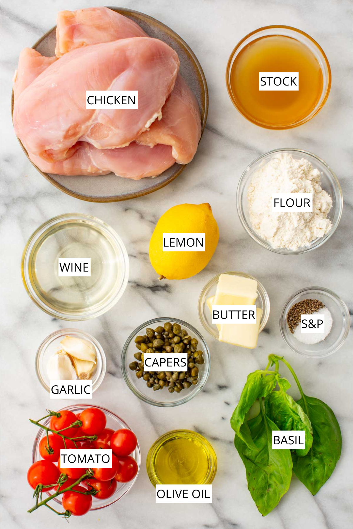 Flat-lay of labeled chicken scallopini ingredients on a marble surface, including raw chicken breasts, chicken stock, all-purpose flour, white wine, lemon, butter, salt and pepper, garlic cloves, capers, cherry tomatoes on the vine, olive oil, and fresh basil.