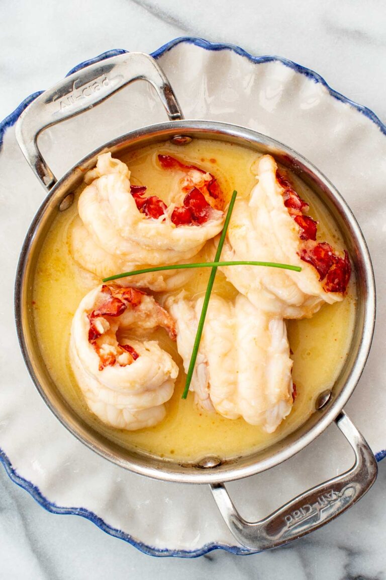 Butter poached lobster plated in a metal pot with two chives sprigs on top.