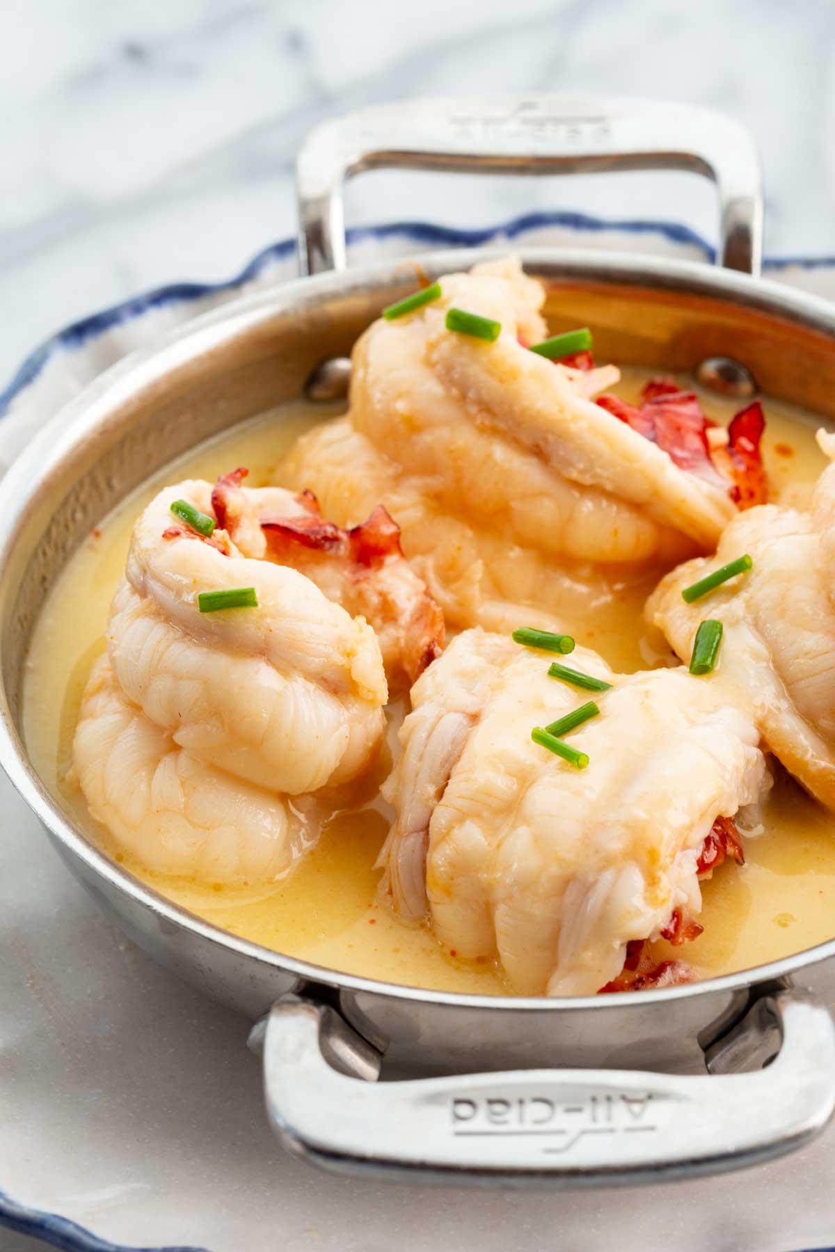 Side view of butter poached lobster plated on a silver dish and a white background.