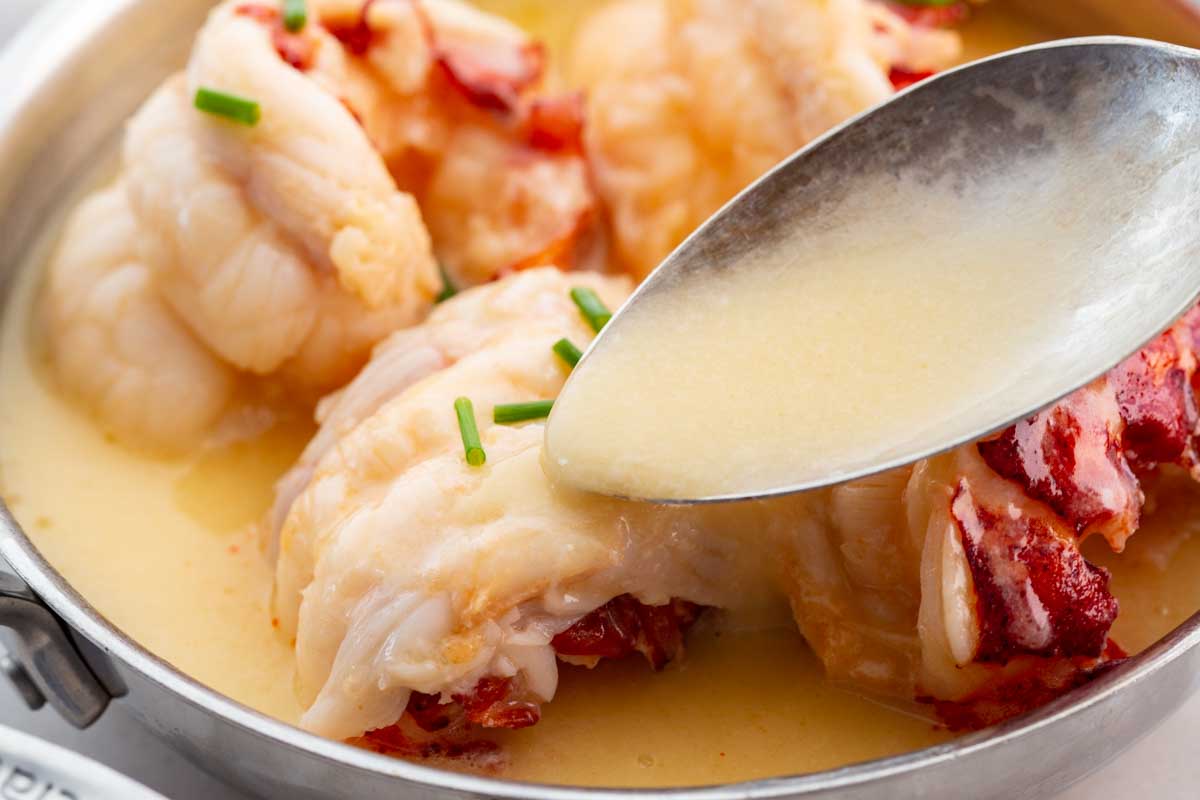 Butter sauce being spooned over a cooked lobster tail.