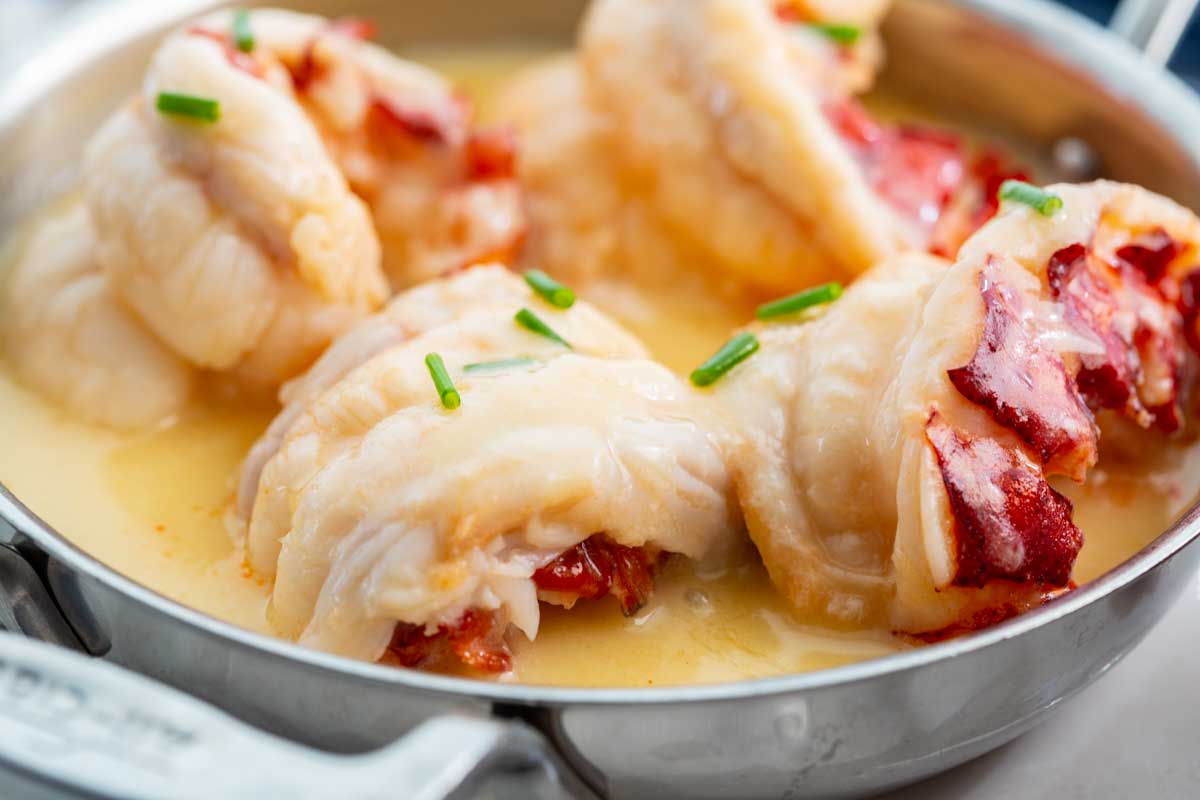 Silver dish with butter poached lobster with pieces of chives.