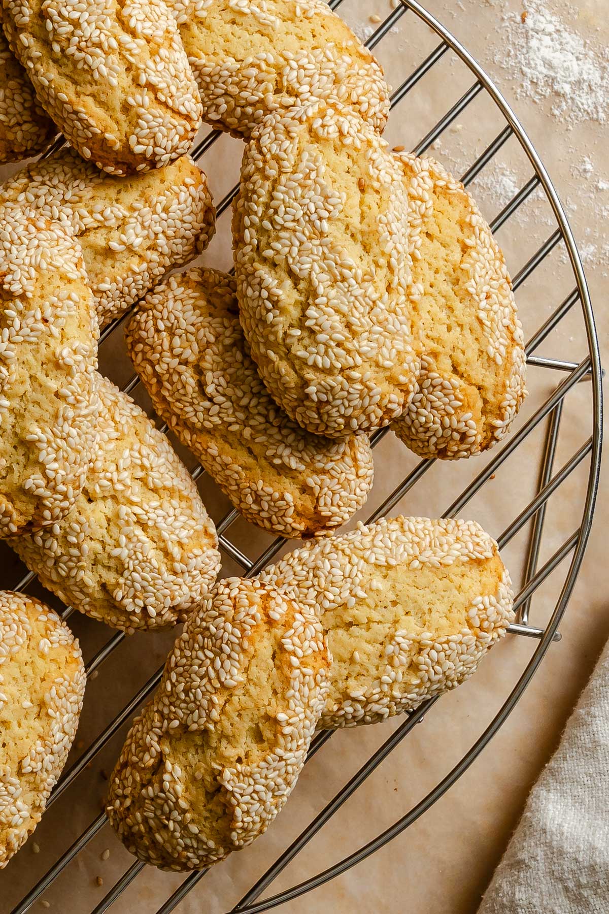 Close-up overhead shot of Italian sesame seed cookies stacked on a round wire cooling rack, showing their oval shape and dense coating of toasted sesame seeds with a golden-baked exterior.