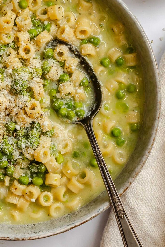 Close up of pasta e piselli in a shallow bowl with a spoon scooping ditalini, peas and broth.
