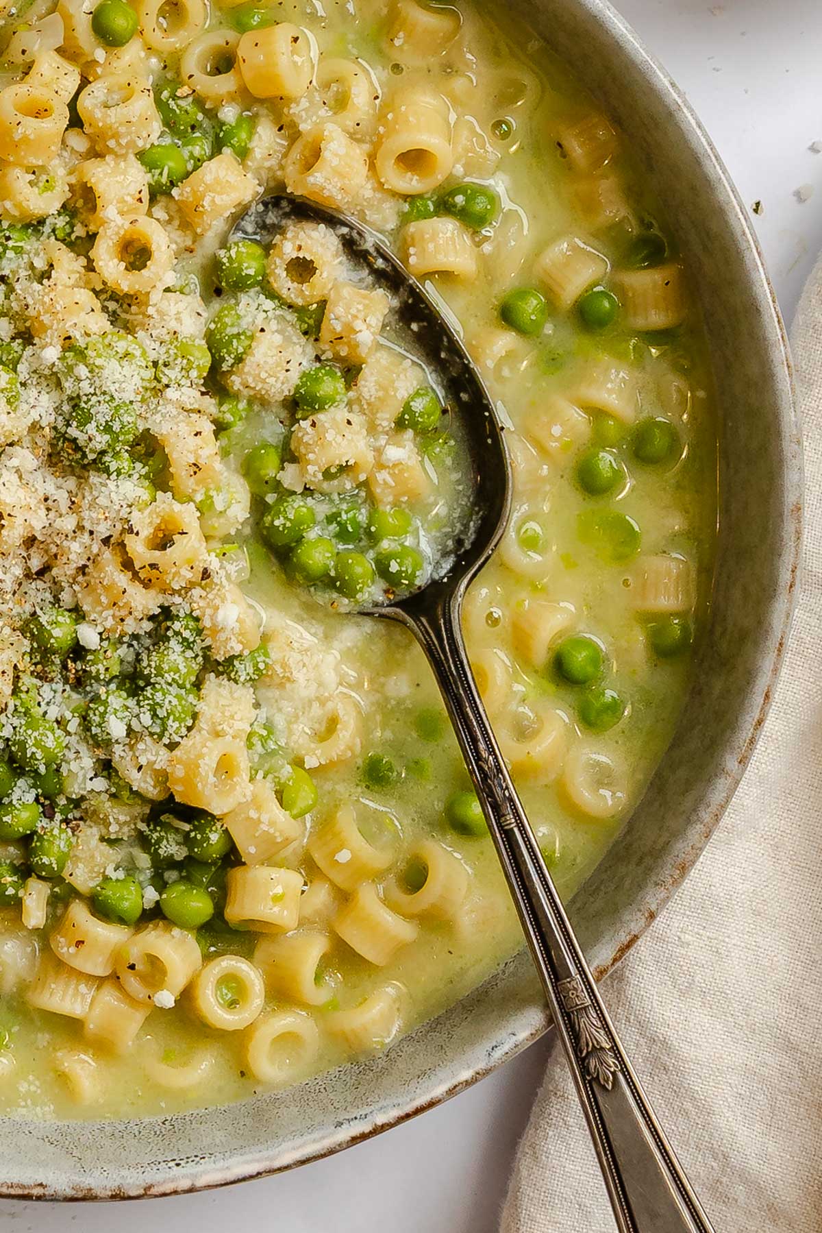 Close up of pasta e piselli in a shallow bowl with a spoon scooping ditalini, peas and broth.