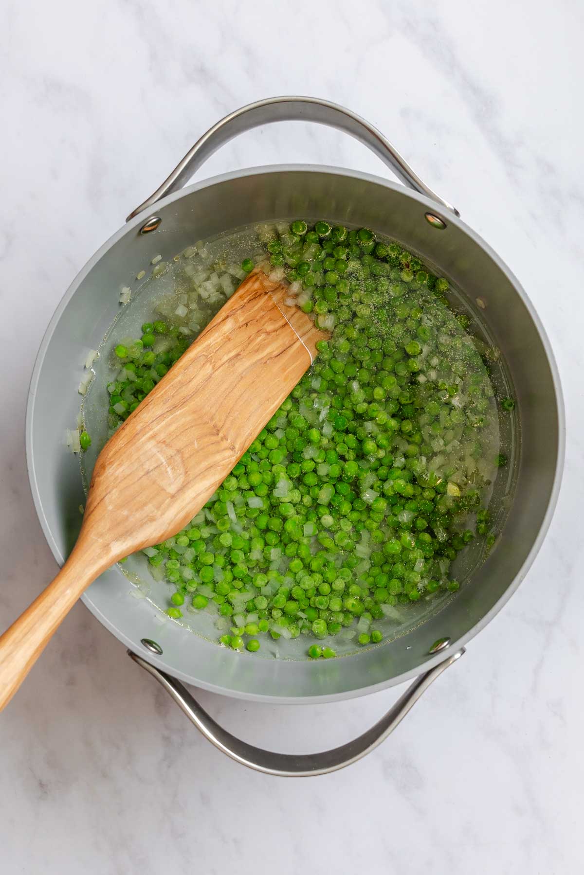 Peas and water added to a pot with onions.