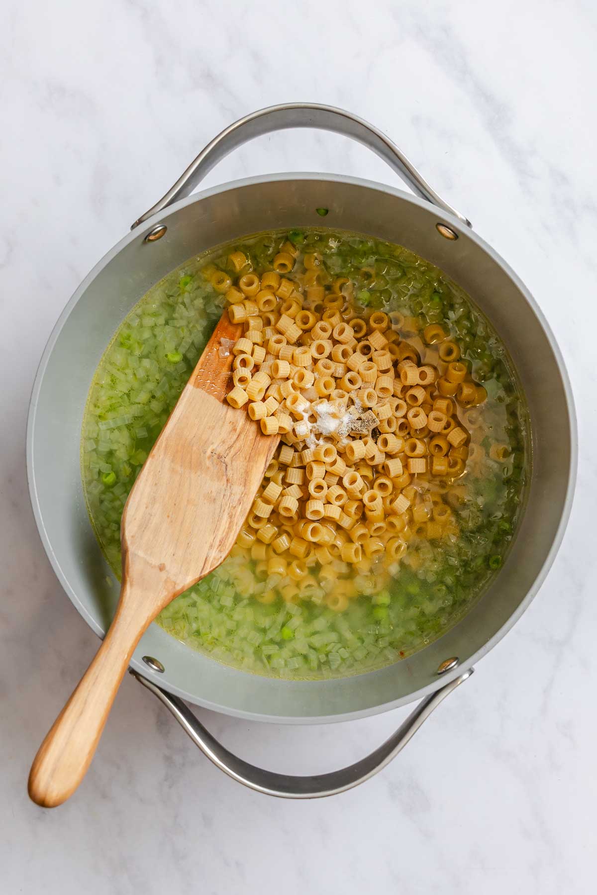 Ditalini pasta, salt and pepper added to a gray pot with peas.