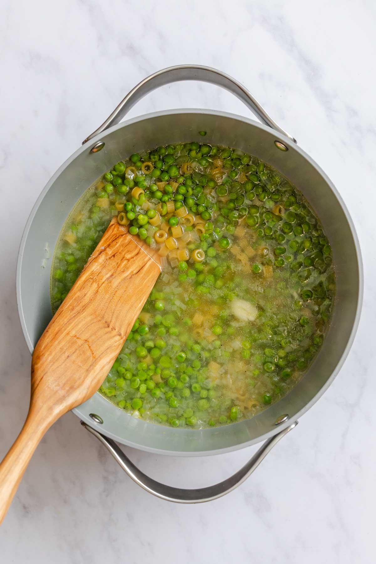Gray pot filled with pasta, stock and peas being cooked.