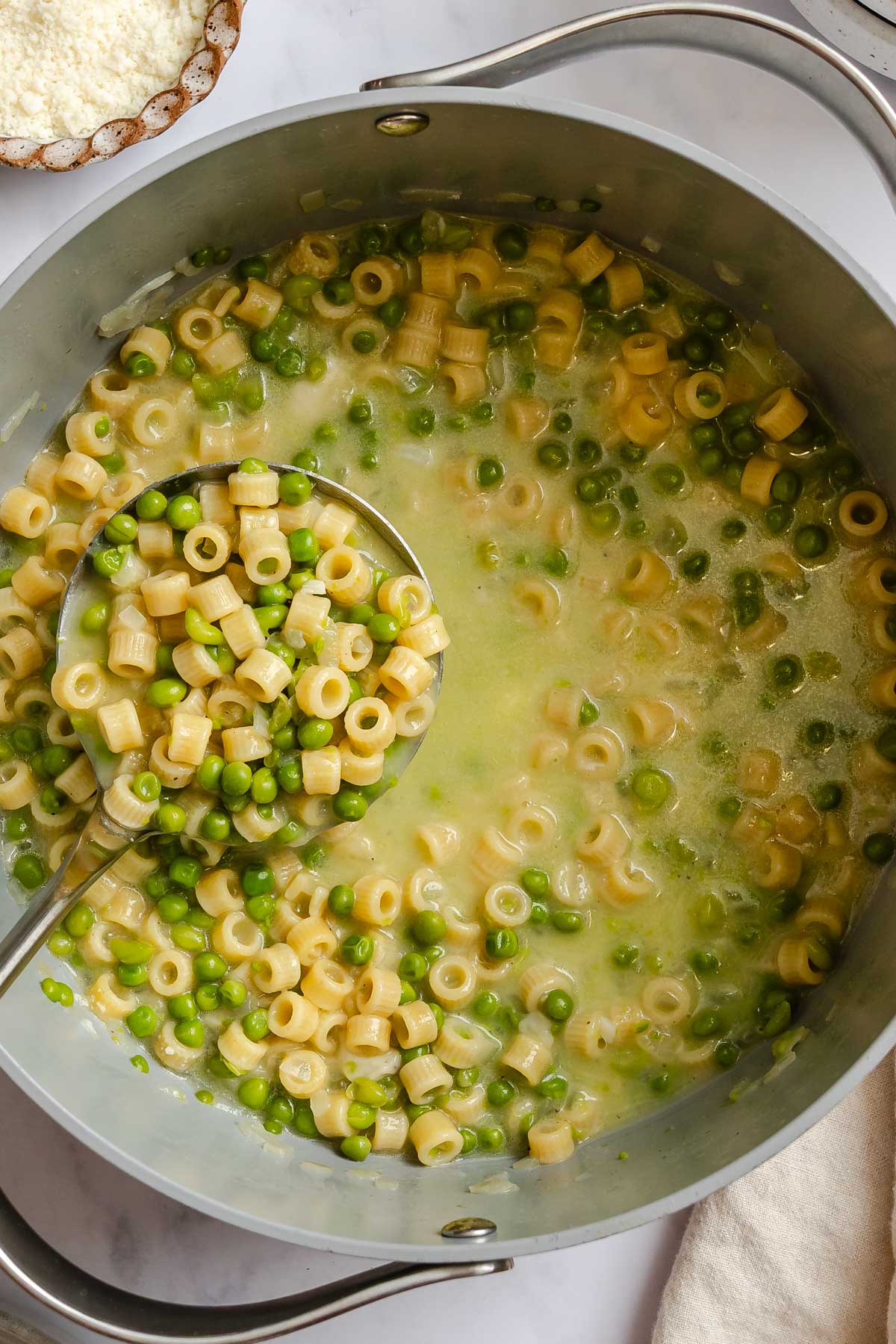 Top view of pot of pasta e piselli with a ladle.