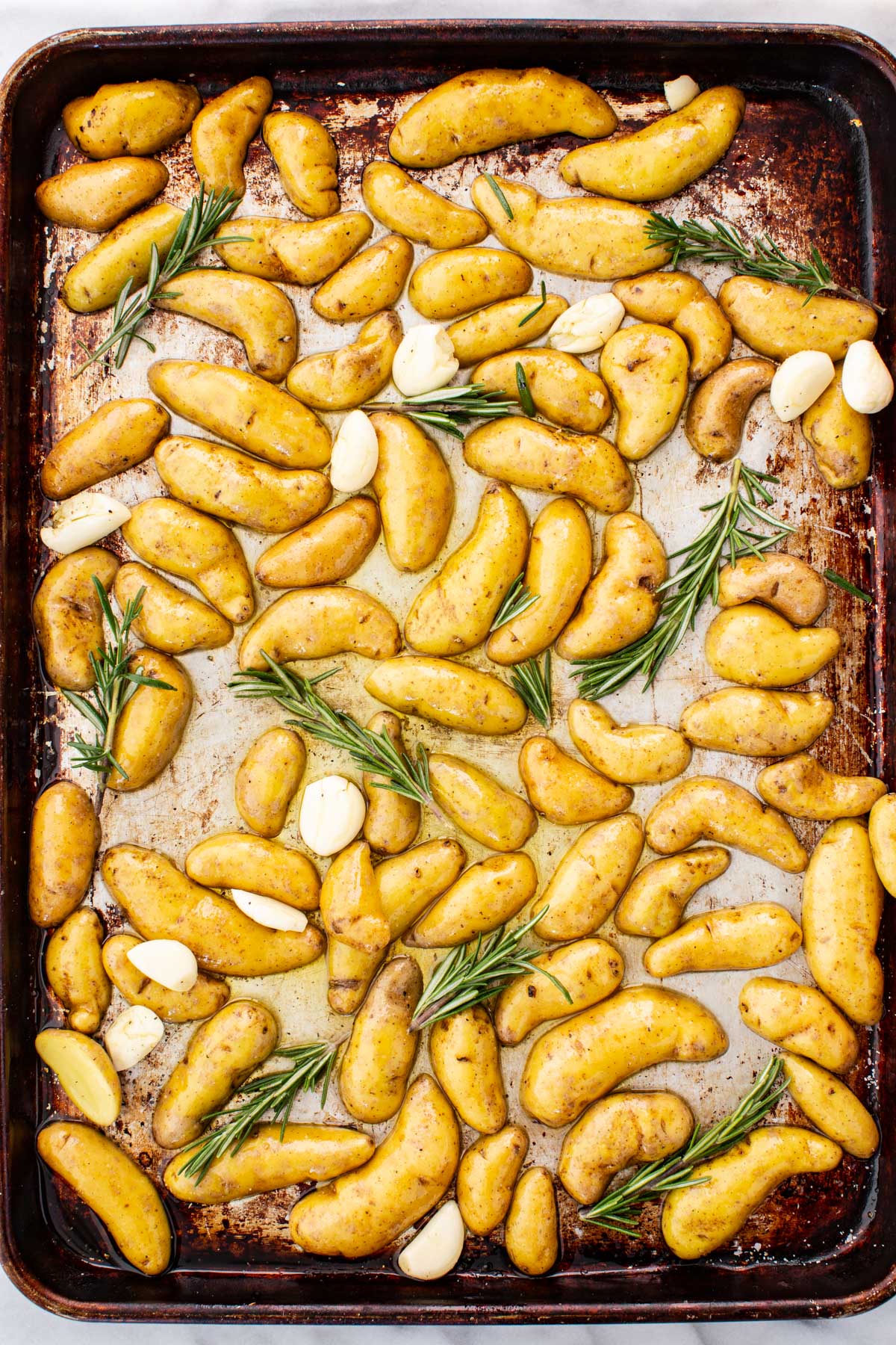 Halved roasted fingerling potatoes ina sheet pan with garlic cloves and rosemary sprigs.