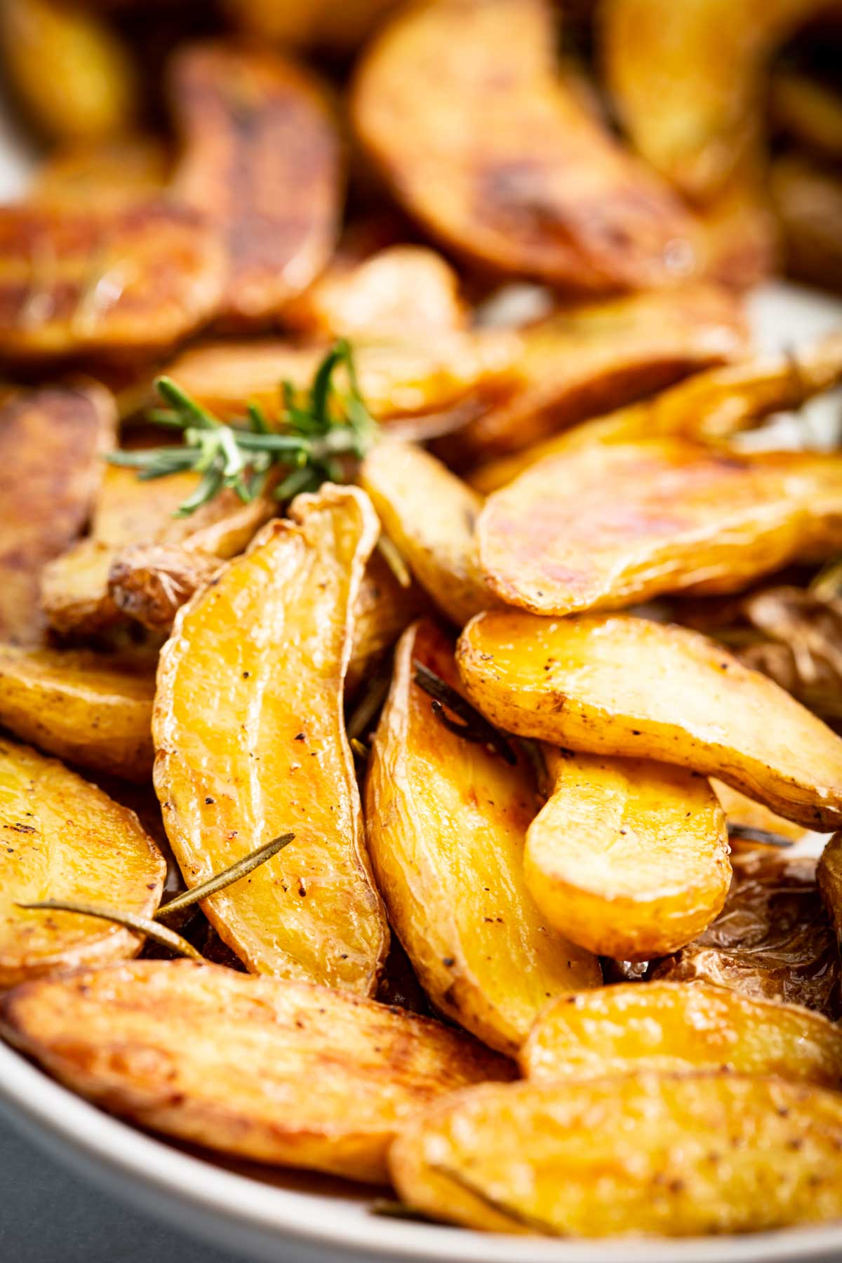 Close up of golden roasted fingerling potatoes with crispy browned edges, rosemary and garlic.