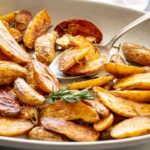 Crispy roasted fingerling potatoes with rosemary and garlic served in a shallow bowl with a spoon.