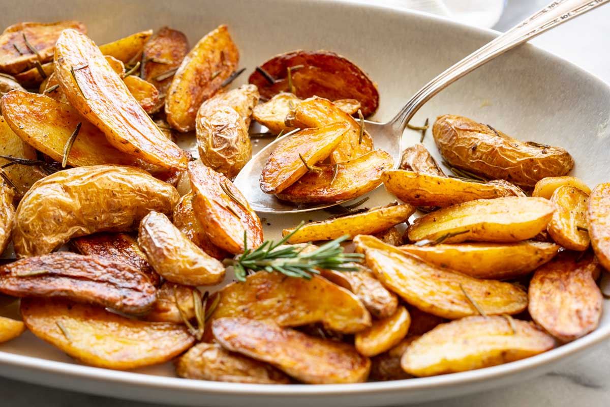 Crispy roasted fingerling potatoes with rosemary and garlic served in a shallow bowl with a spoon.