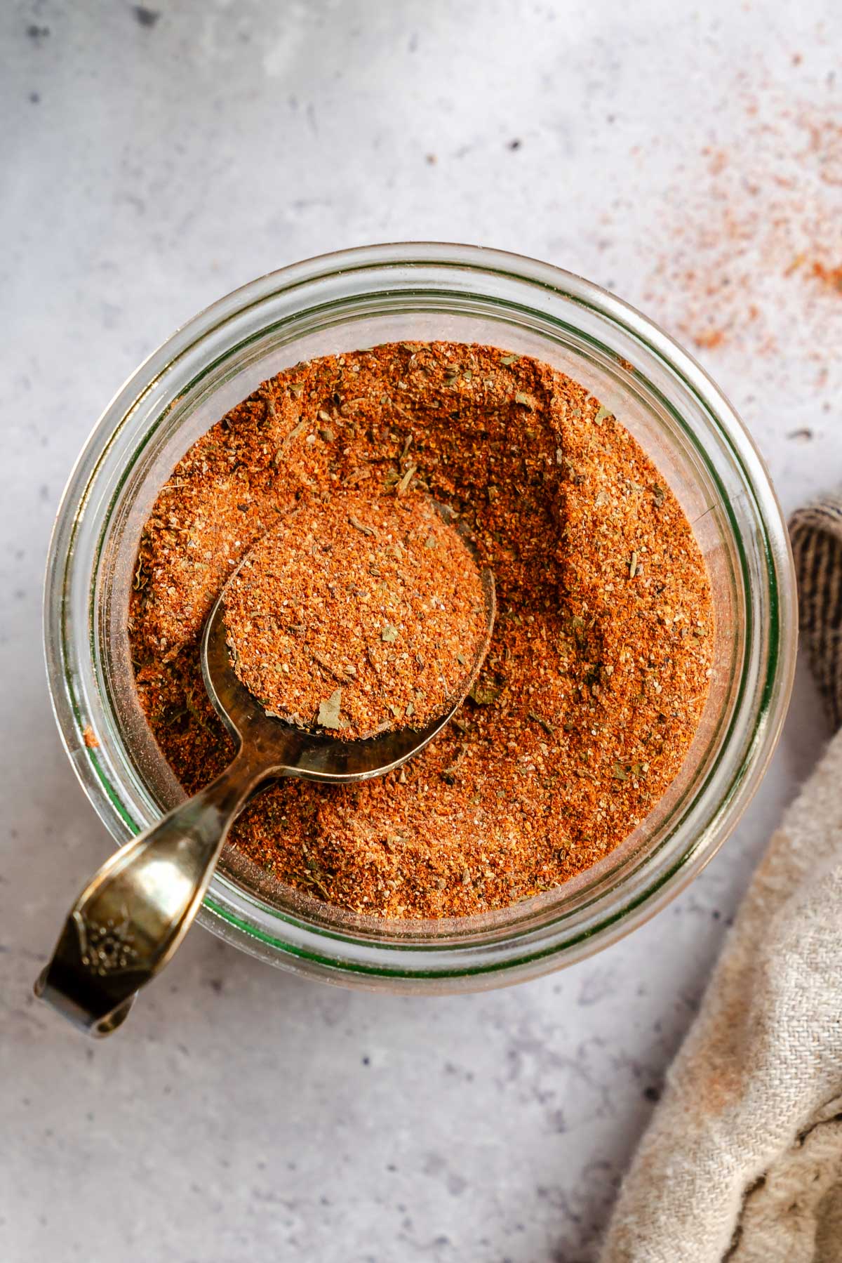 Close-up overhead view of homemade Cajun seasoning in a glass Weck jar, with a vintage measuring spoon scooping the vibrant reddish-orange spice blend.