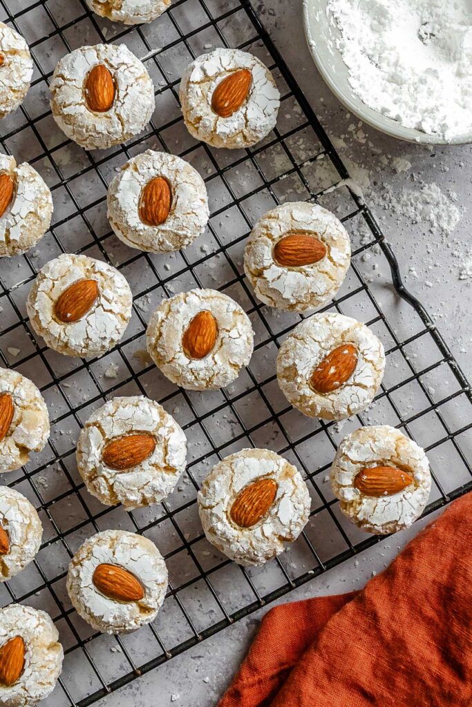 Overhead shot of Sicilian almond cookies over a cookie tray next to powdered sugar and a red kitchen towel.