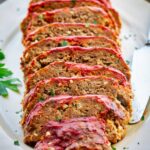 Close-up angled shot of Italian meatloaf slices fanned out on a ceramic platter, highlighting the caramelized tomato glaze, tender crumb texture, and fresh herb garnish.