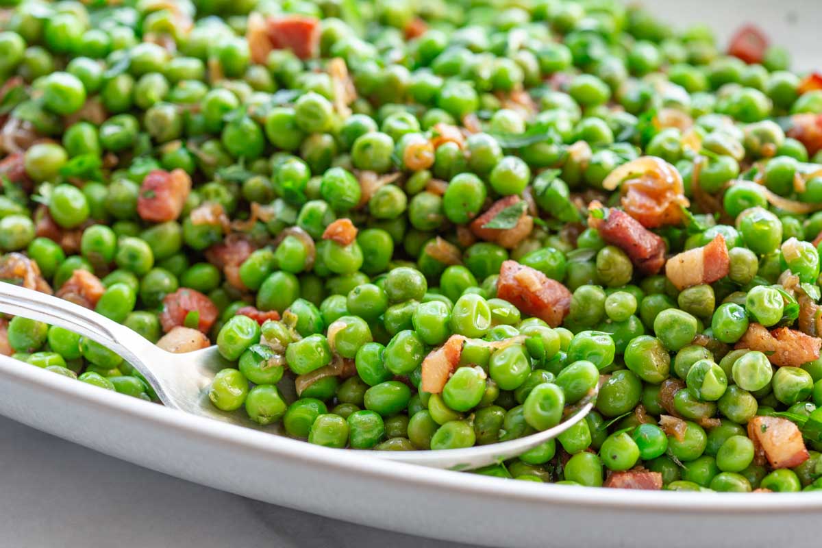 Macro close-up of vibrant green peas mixed with crispy pancetta chunks and caramelized shallots.