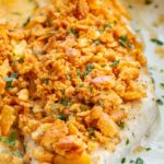 Extreme close-up of a single baked fish fillet, the buttery Ritz cracker crust deeply golden and crunchy, topped with chopped parsley, resting in creamy pan sauce.