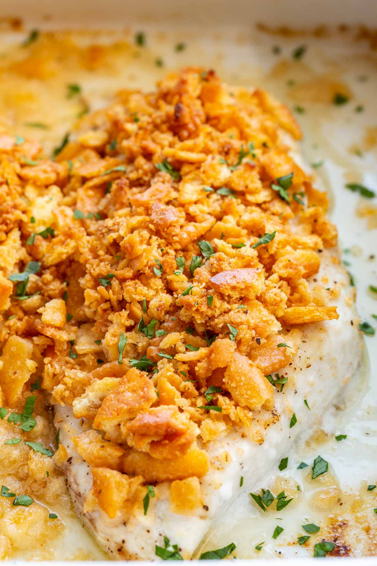 Extreme close-up of a single baked fish fillet, the buttery Ritz cracker crust deeply golden and crunchy, topped with chopped parsley, resting in creamy pan sauce.