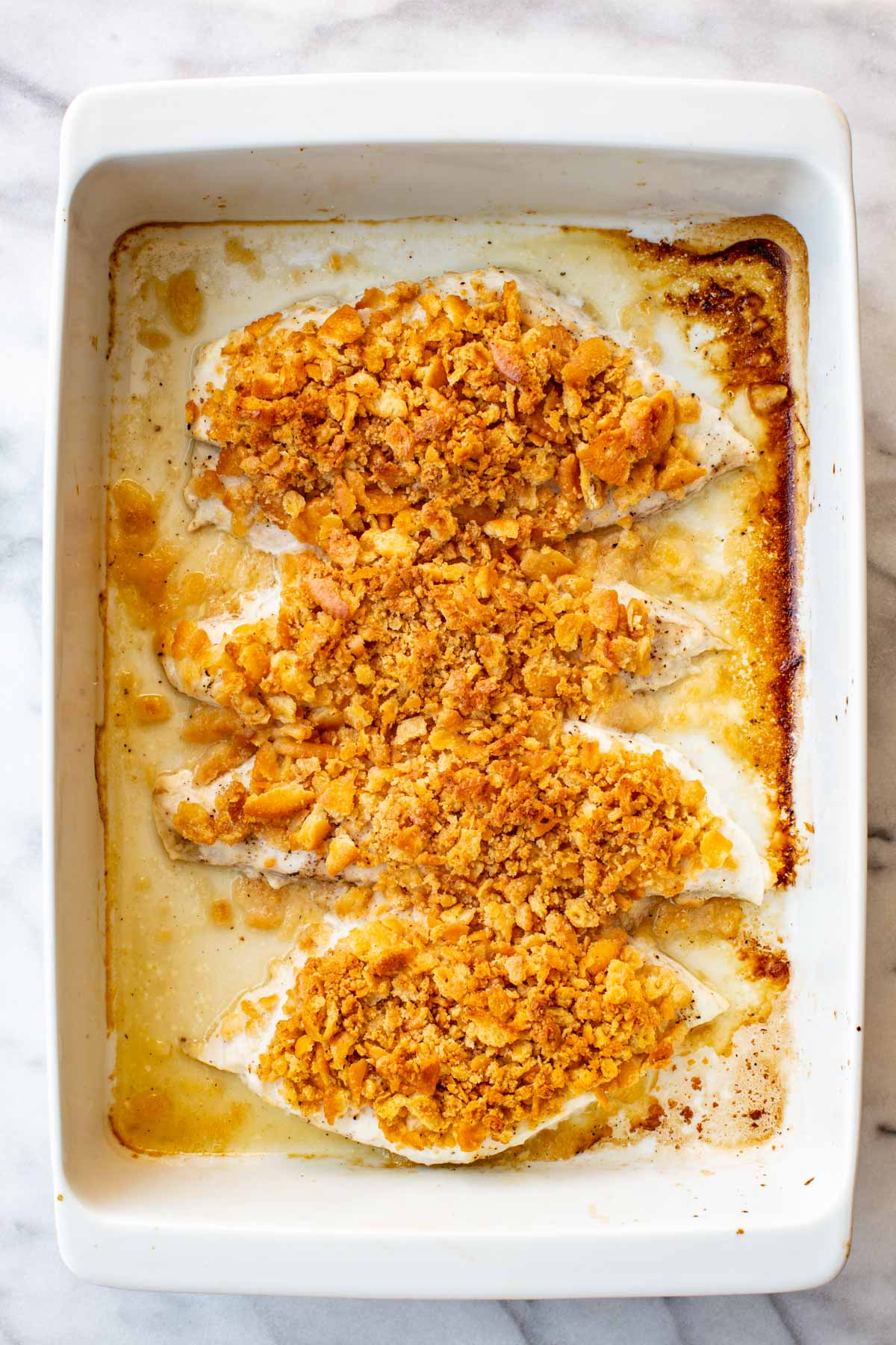 Overhead view of four baked fish fillets in a white baking dish, the Ritz cracker topping golden and lightly crisped, surrounded by bubbling pan juices.