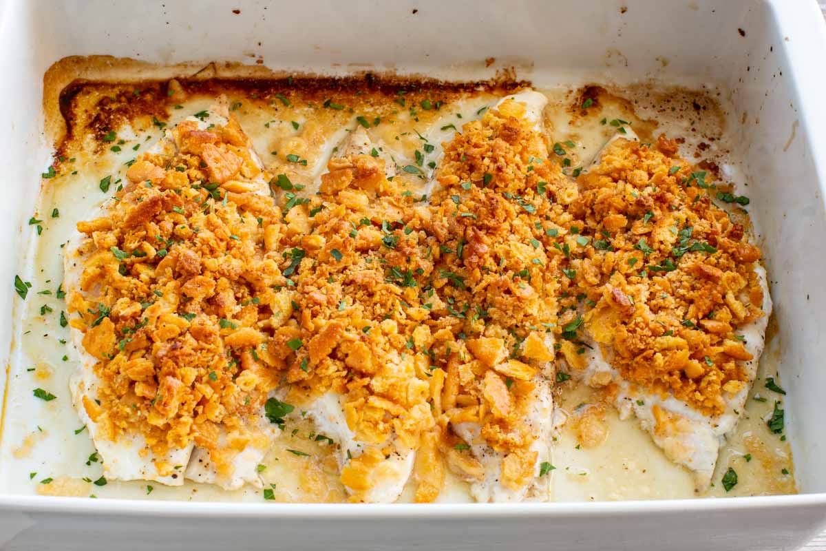 Overhead close-up of four baked fish fillets in a white dish, topped with golden Ritz cracker crumble and garnished with freshly chopped parsley.